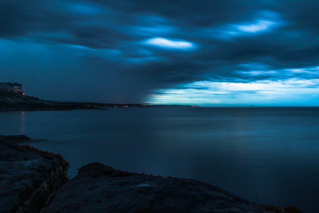 Stormy twilight sky with dark swirling clouds over calm shoreline serene nature wallpaper background
