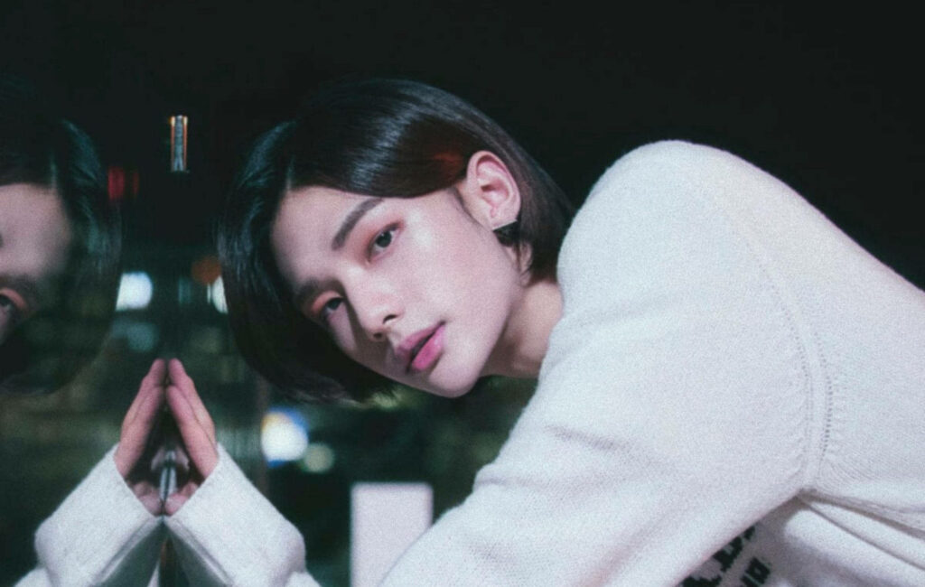 Stray Kids member posing thoughtfully against glass reflection city lights blurred background wallpaper