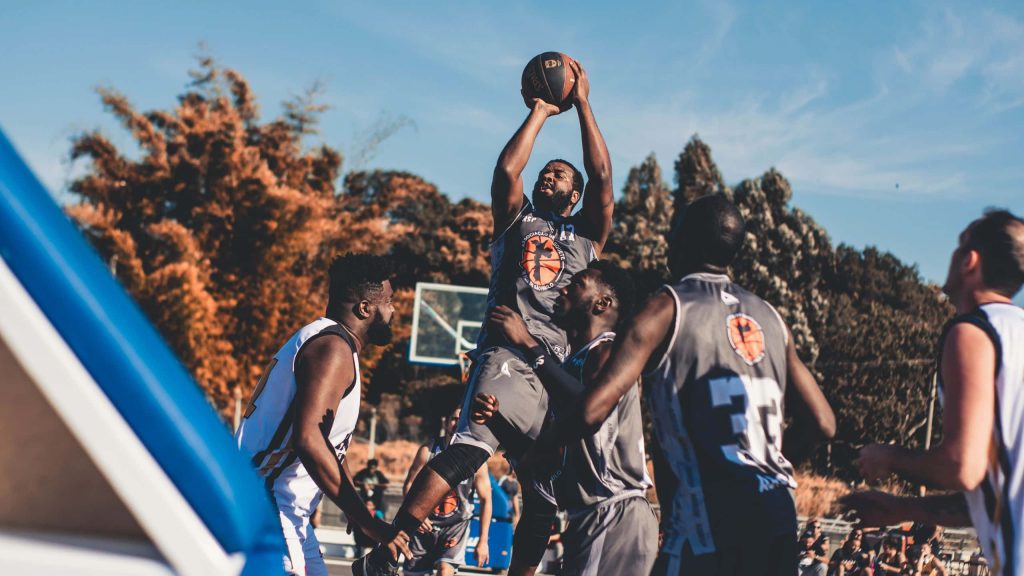 Adult athletes competing in intense street basketball game on outdoor court under clear sky Wallpaper
