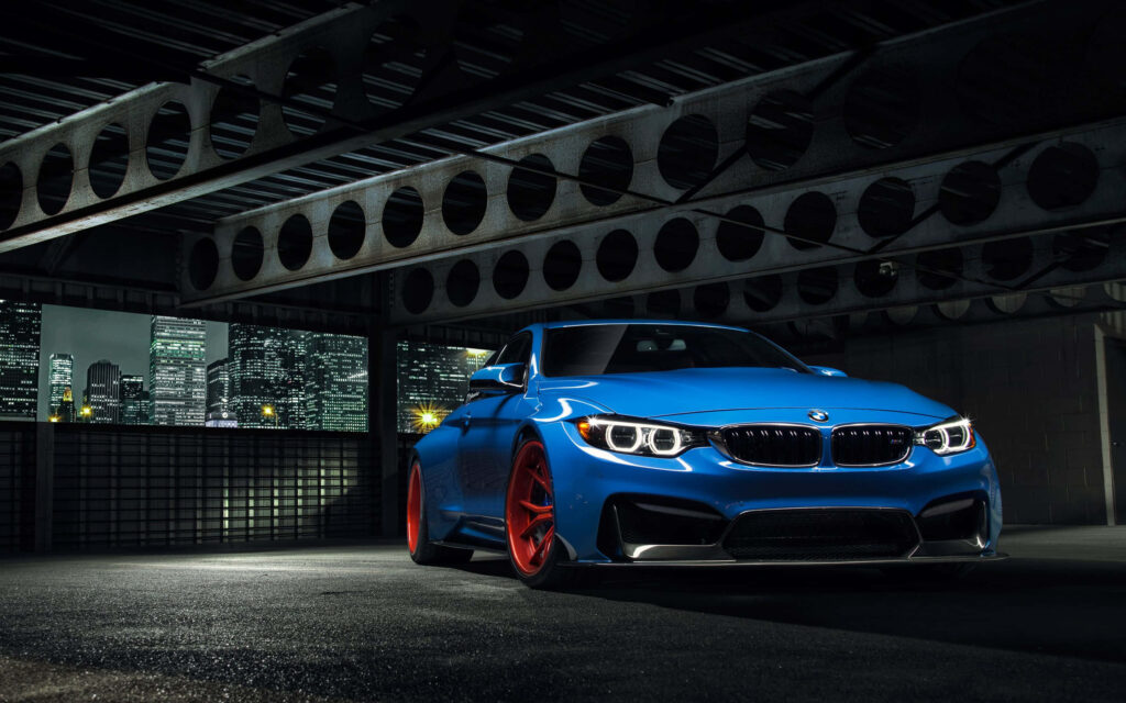 Blue BMW with red rims parked under industrial structure city skyline night wallpaper background