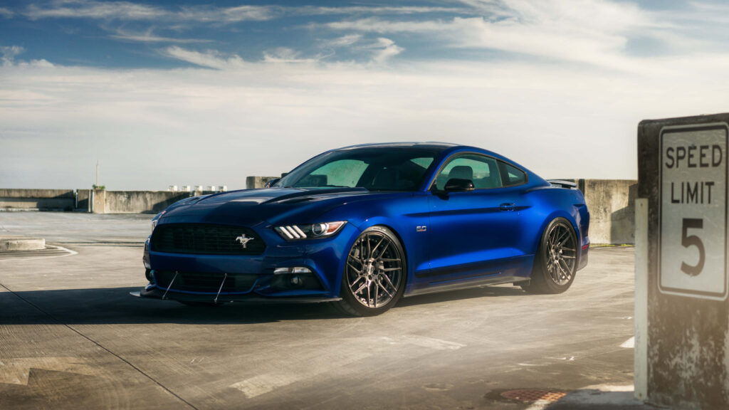 Blue Ford Mustang GT parked on rooftop beside speed limit sign under colorful sky wallpaper