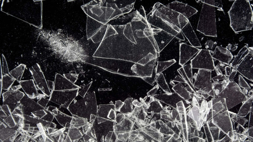 Broken glass wallpaper with sharp transparent shards on dark background for edgy design themes