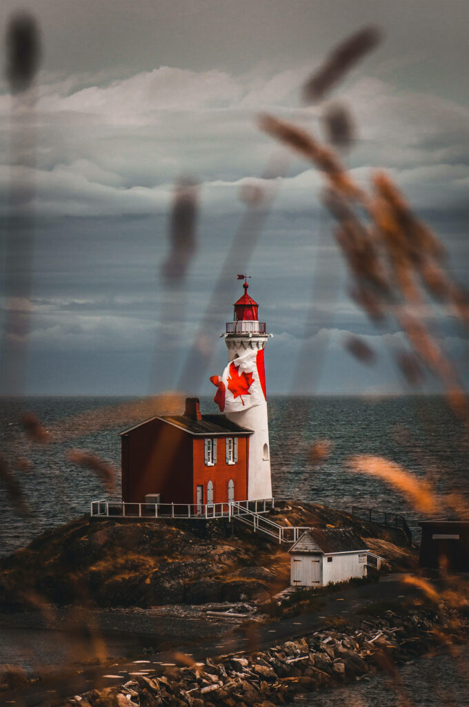 Canadian lighthouse with red white maple leaf flag on green field by dramatic cloudy seascape Wallpaper