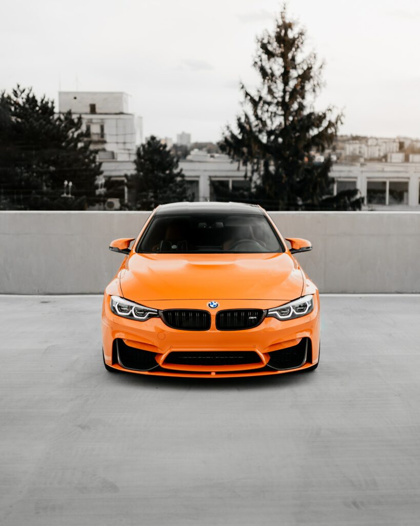 Vibrant Orange BMW on Rooftop: Urban Skyline Wallpaper
