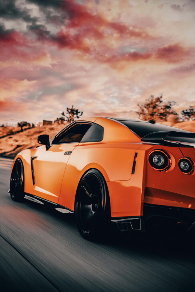 Orange Nissan R35 GTR speeding on road with dramatic vibrant sunset clouds background wallpaper