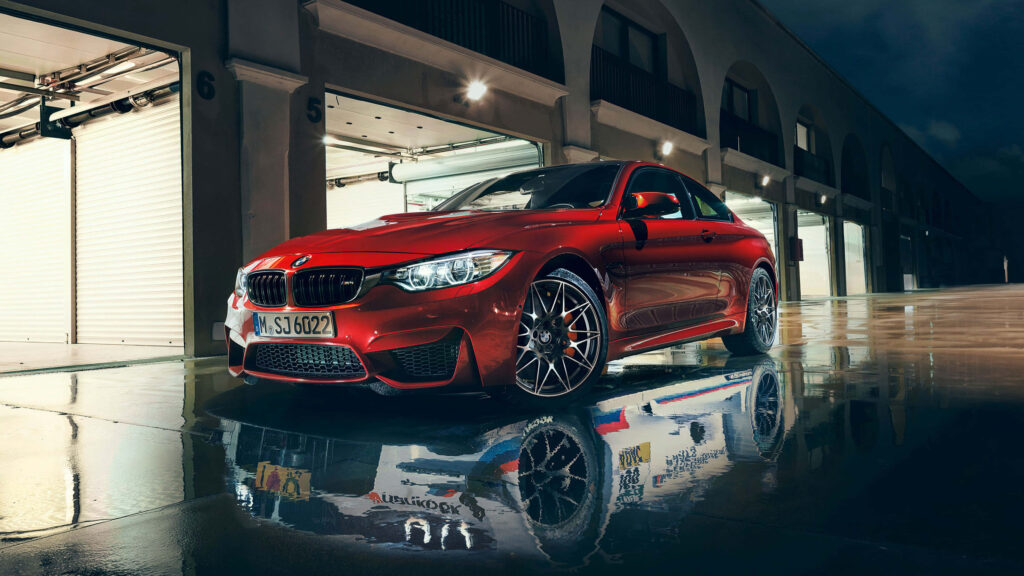 Red BMW parked at night with white reflections on wet pavement in front of garage doors Wallpaper