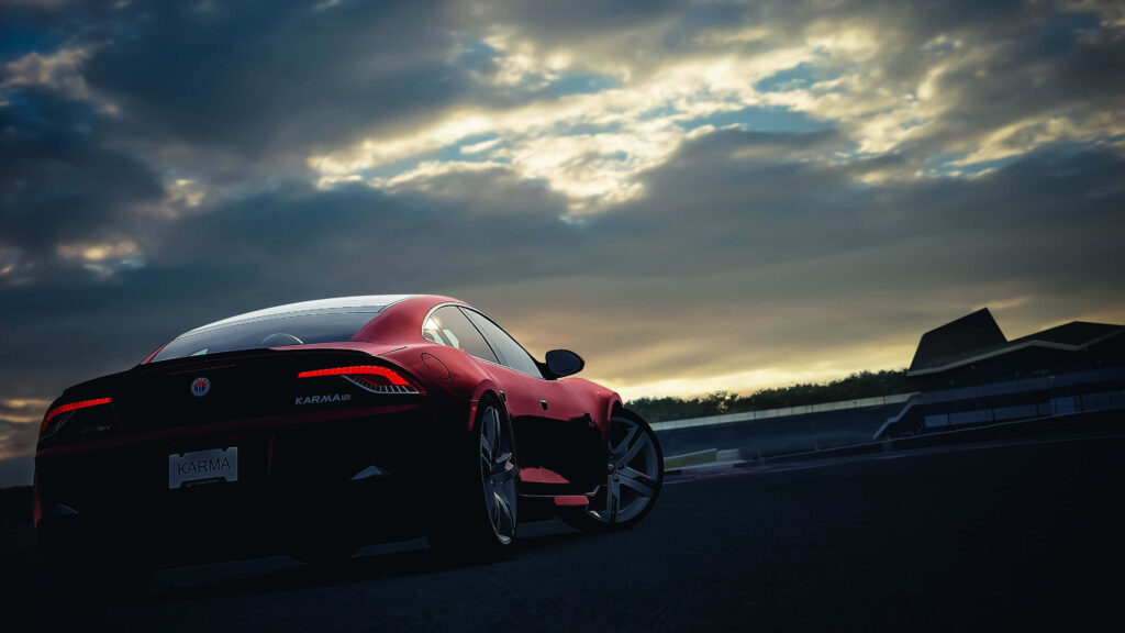 Red Fisker Atlantic car displayed on modern racetrack under dramatic cloudy sky wallpaper background