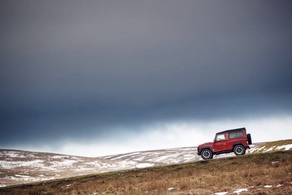 Red Land Rover V8 on Grassy Slope: Adventure-Ready Wallpaper
