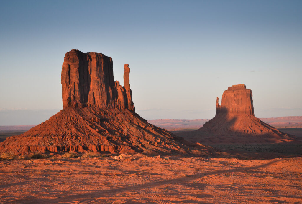 Sunlit red rock formations rising in vast desert with clear blue sky wallpaper background