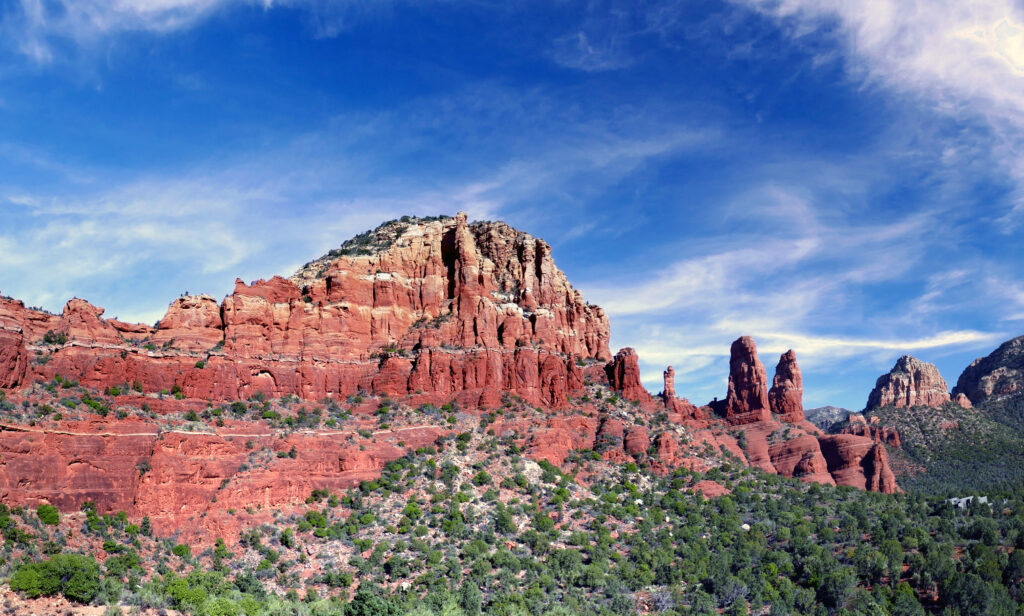 Red rock formations above green slopes under vibrant blue sky with wispy clouds landscape wallpaper