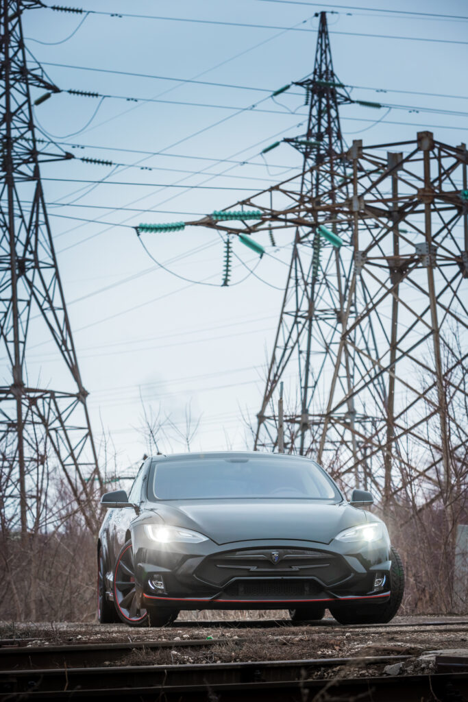 Sleek Tesla Model S Wallpaper with Industrial Power Lines Background