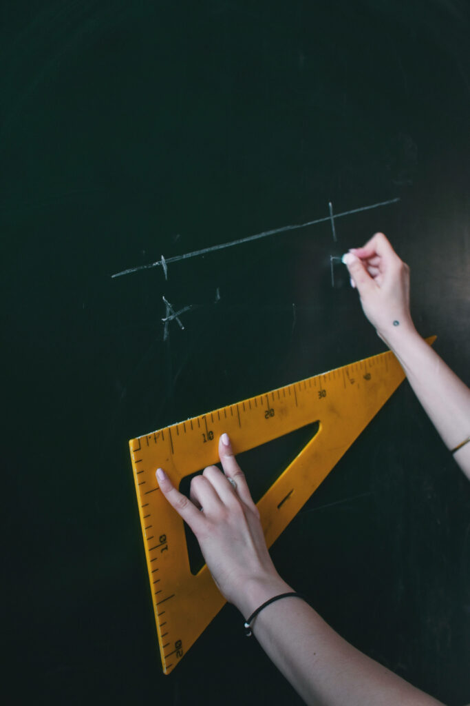 Student drawing geometric lines with yellow triangular ruler on dark green chalkboard in classroom Wallpaper