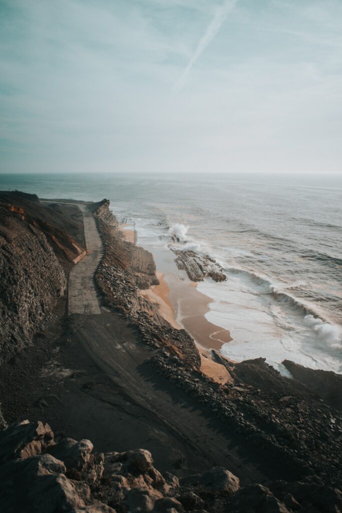 Aerial view of rugged coastline with winding cliff road and waves crashing on sandy shore wallpaper