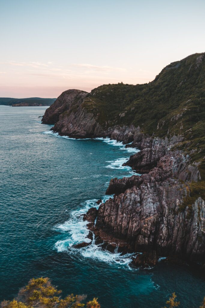Aerial view of rugged cliffs and deep blue sea with waves breaking in soft evening light wallpaper