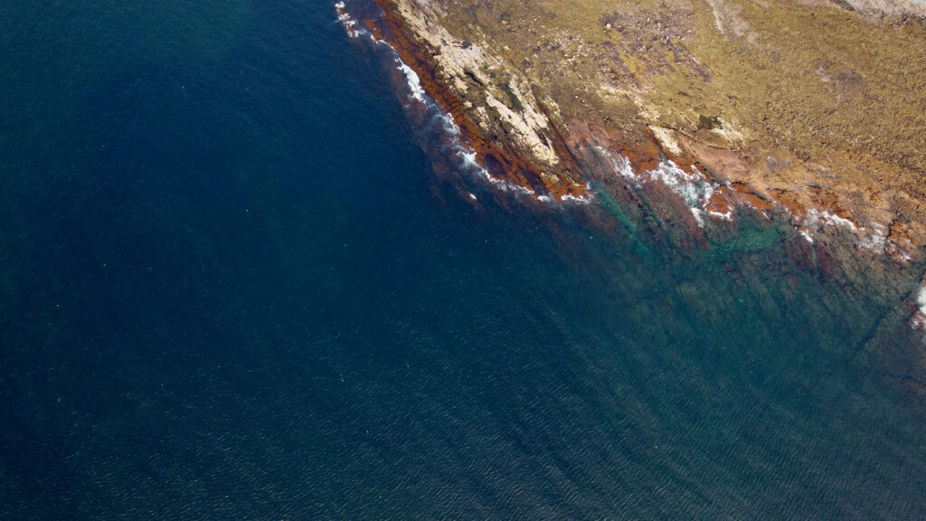 Aerial view of rugged coastline with clear deep blue sea and textured rocky shore wallpaper background