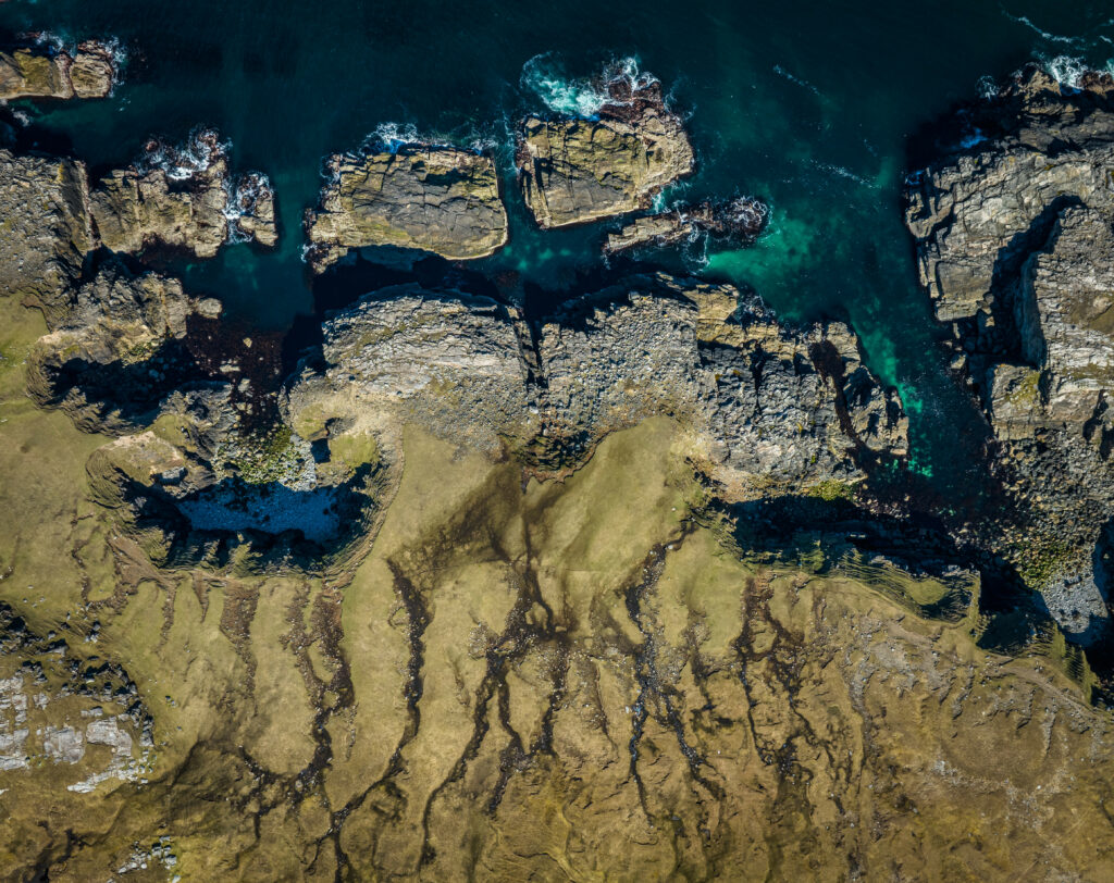 Aerial view of rugged coastline with deep blue ocean water rocky outcrops and green terrain Wallpaper