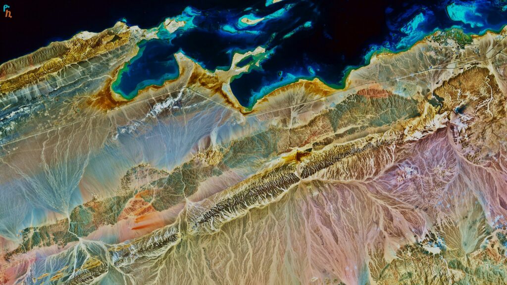 Aerial view of rugged coastline with vivid earth tones and turquoise sea geological formations wallpaper