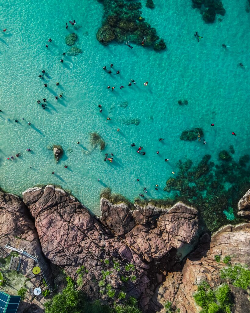Aerial view of vibrant coastline with turquoise waters rugged rocks and people enjoying the sea Wallpaper