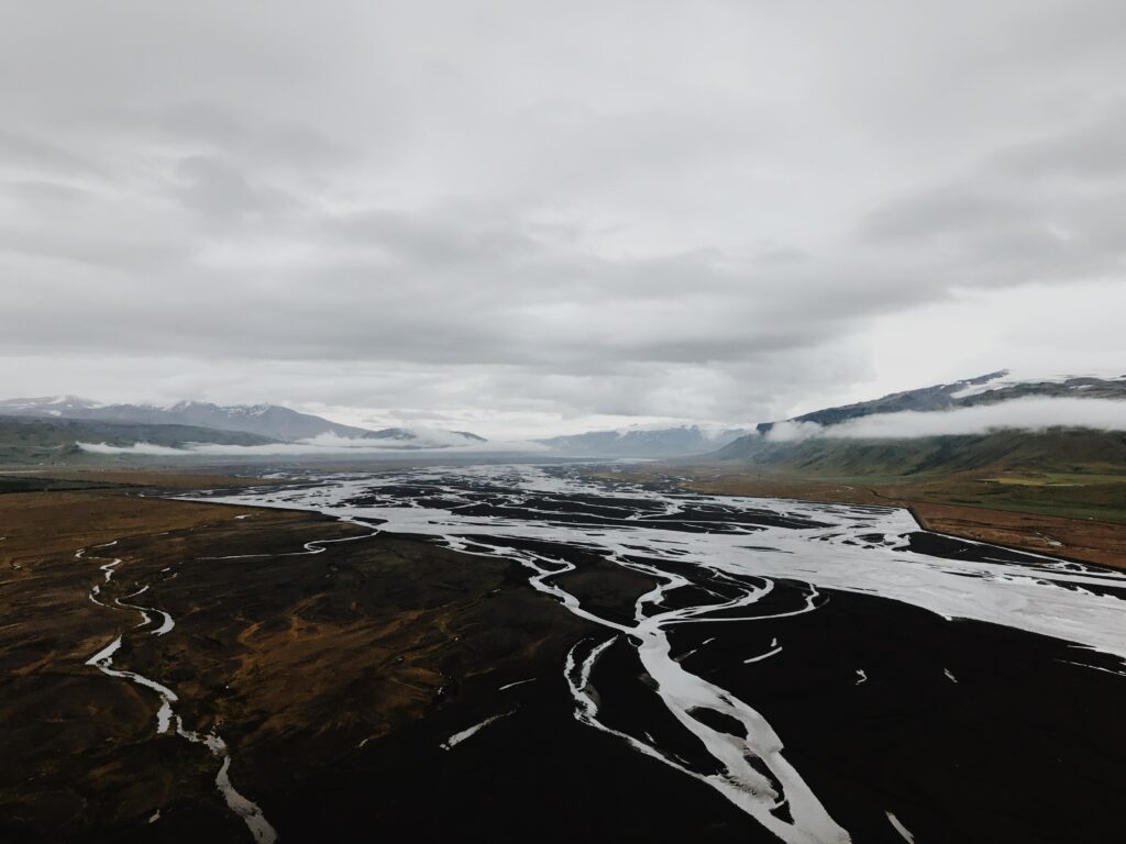 Aerial view of winding river through rugged mountain valley with scattered clouds and earthy tones Wallpaper