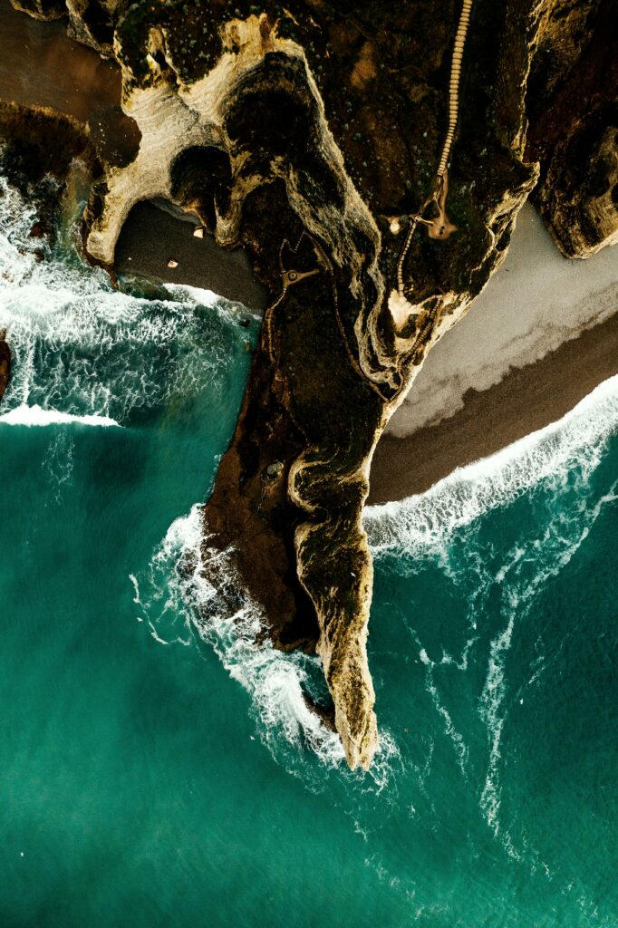 Aerial view of rugged cliffs and turquoise sea with foamy waves on a secluded beach wallpaper