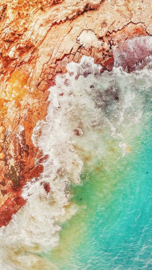 Aerial view of orange cliffs and turquoise ocean waves with white sea foam for iPhone wallpaper