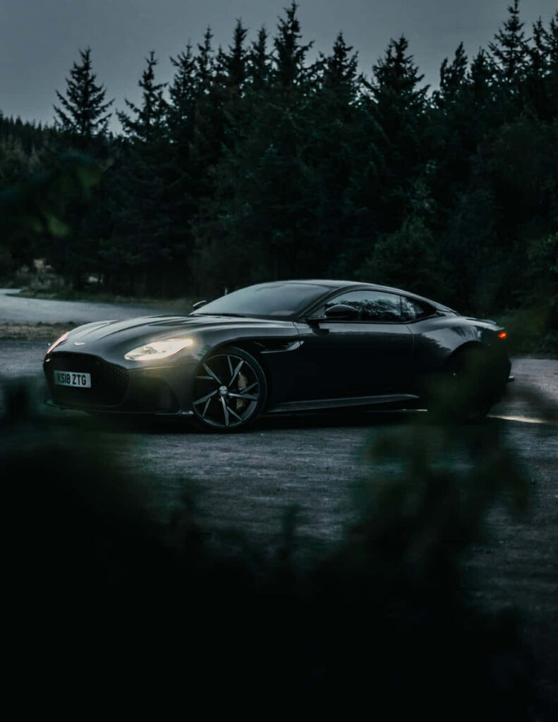 Elegant Aston Martin Wallpaper: Sleek Black Sports Car in Forest