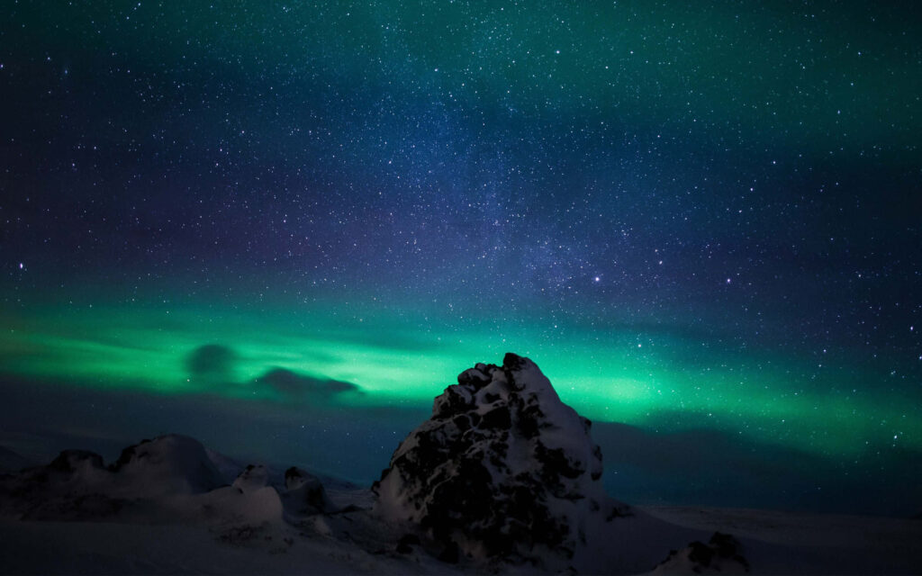 Stunning Aurora Borealis Over Starry Sky: Snowy Rocks Wallpaper