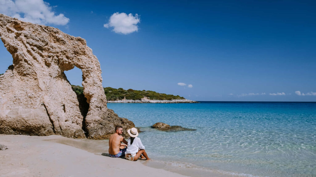 Couple by Unique Rock on Tranquil Greek Beach - Stunning Scene Wallpaper