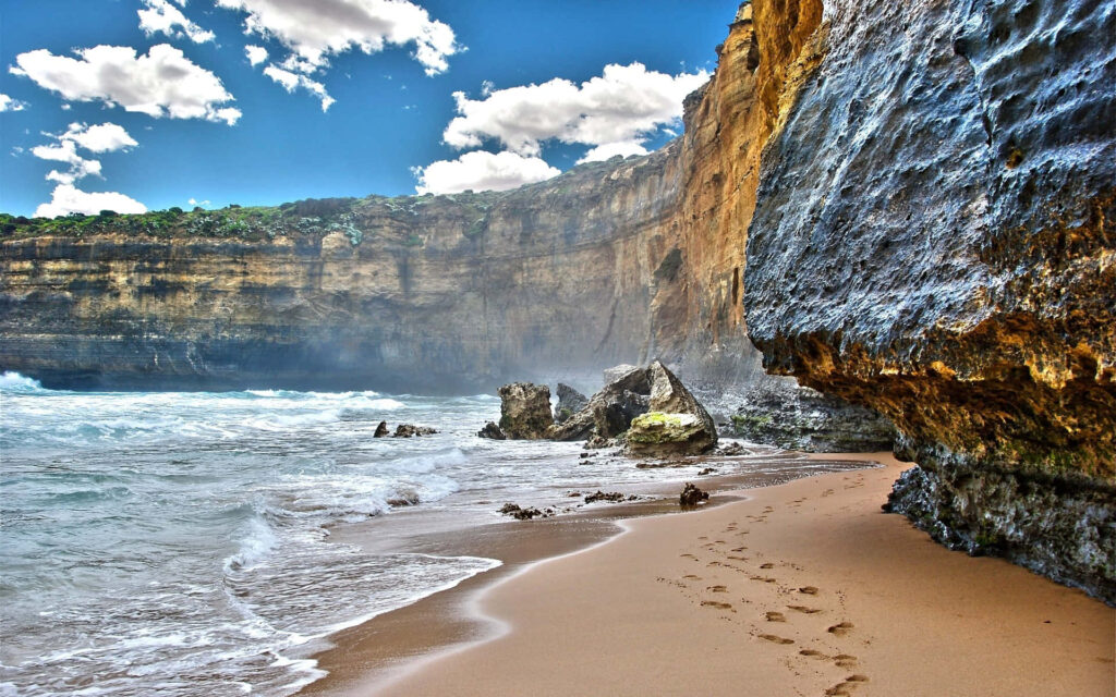 Stunning Beach Scene: Rugged Mountain Cliff & Calm Waves Under Blue Sky Wallpaper