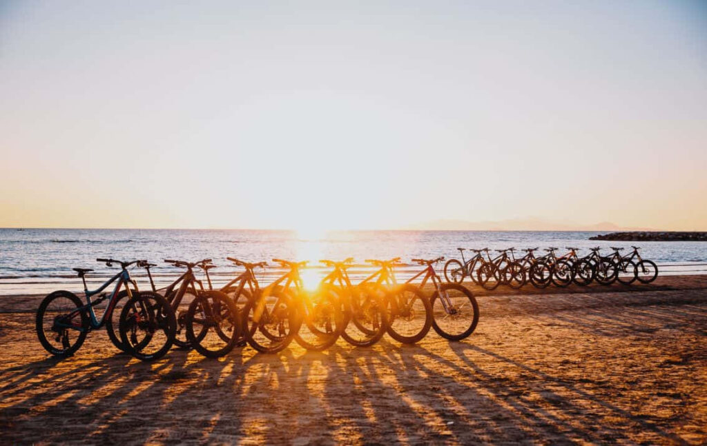 Stunning Beach Sunset: Bikes Lined Up on Sandy Shore at Dusk Wallpaper