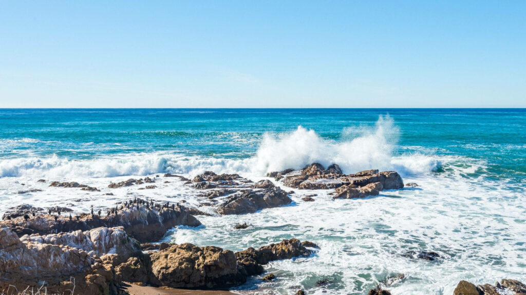 Stunning Beach Wallpaper: Waves & Rocky Formations Under Clear Sky