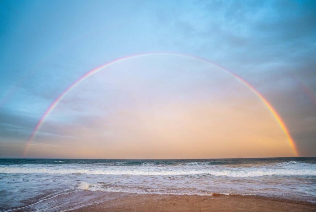 Serene Beachscape: Vibrant Rainbow Over Tranquil Ocean and Sky Wallpaper