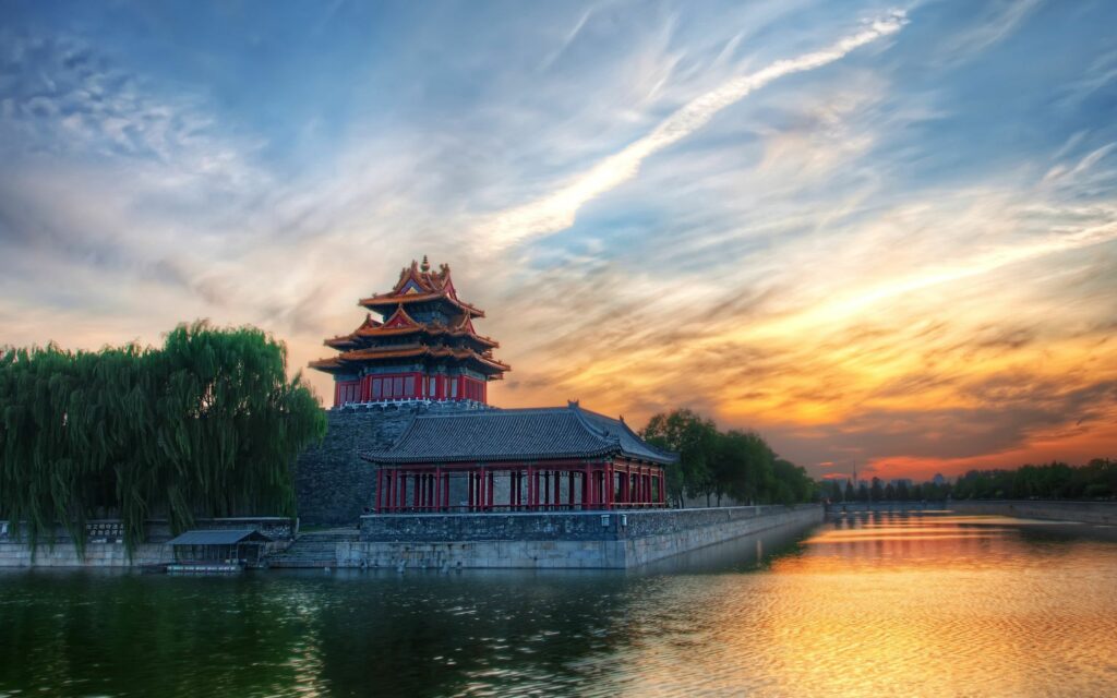 Traditional Beijing architecture at sunset with swirling clouds lush trees and water reflection Wallpaper
