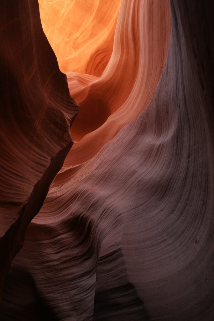 Brown rock formations inside cave with natural light highlighting textured layered walls wallpaper background