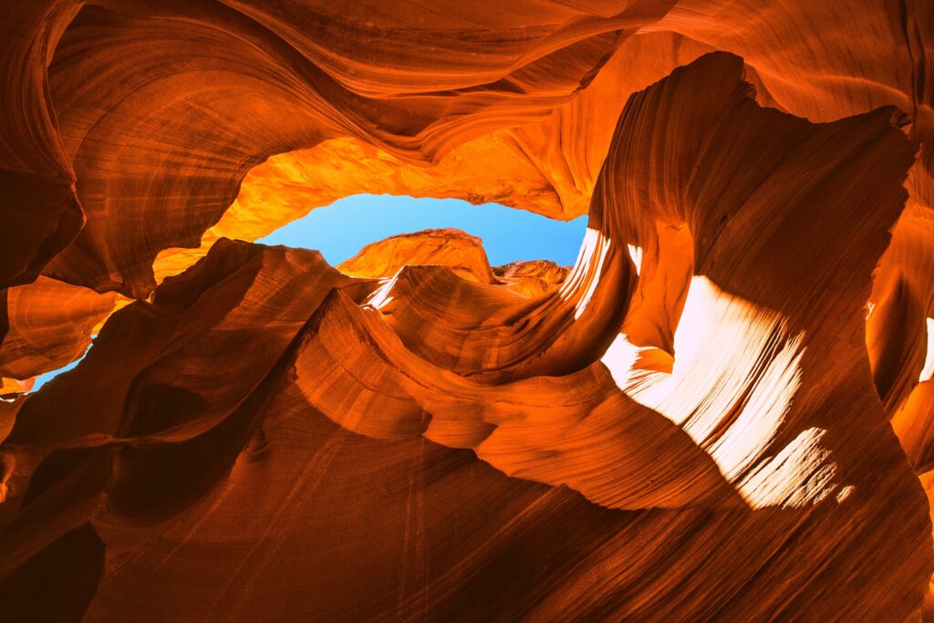 Bottom view of canyon cave with smooth orange rocks sunlight and blue sky background wallpaper