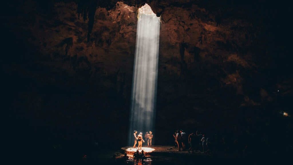 Tourists Awed by Dramatic Light in Stunning Dark Cave Formation Wallpaper