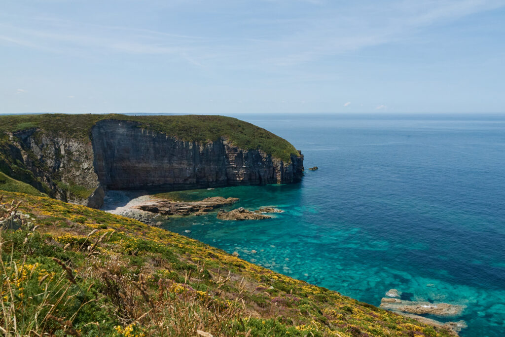 Coastal landscape with rugged cliffs grassy slope and turquoise sea under clear blue sky wallpaper