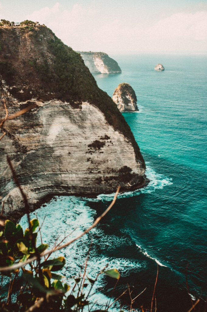 Stunning coastal cliffs with turquoise sea waves crashing rocky shoreline and lush greenery Wallpaper