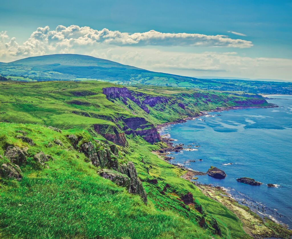 Coastal landscape wallpaper with rocky shore green cliffs blue sea and clear bright sky background