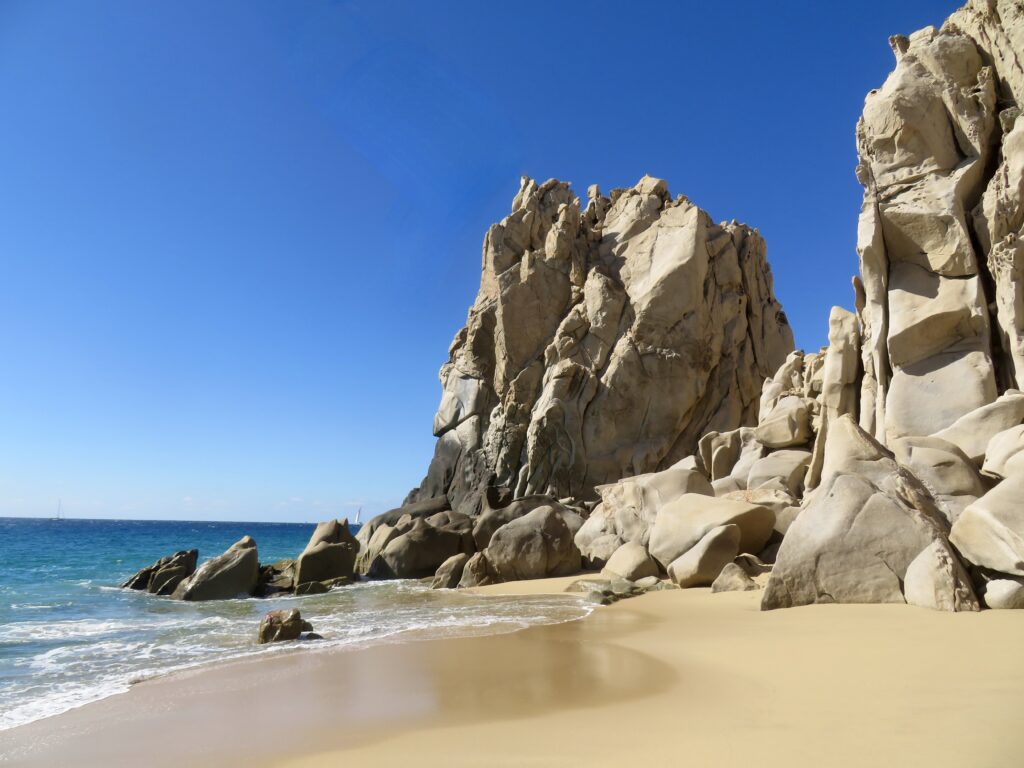 Stunning coastal landscape with rugged rocks golden sand gentle waves and vivid blue sky background Wallpaper