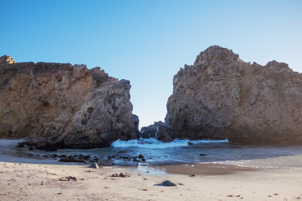 Stunning coastal landscape with rugged rocks and gentle waves under a clear blue sky wallpaper