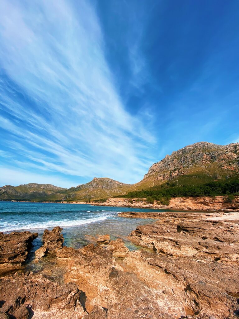 Coastal landscape wallpaper with rugged rocks clear sea gentle waves blue sky and green mountains
