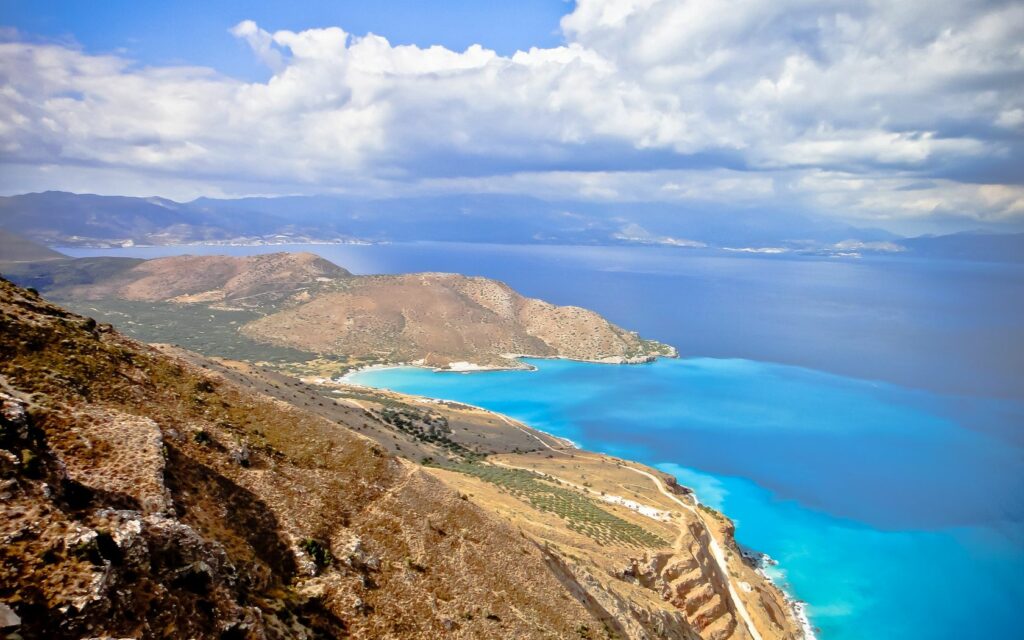 Coastal landscape with vibrant blue ocean and rugged brown hills under clear sky wallpaper