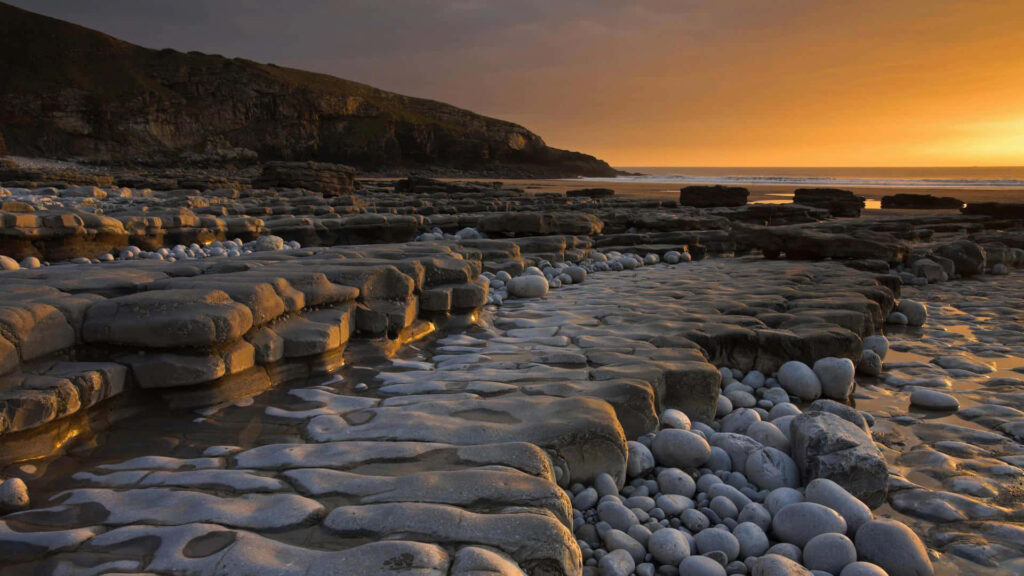Coastal Sunset: Stunning Landscape with Smooth Rocks & Golden Glow Wallpaper