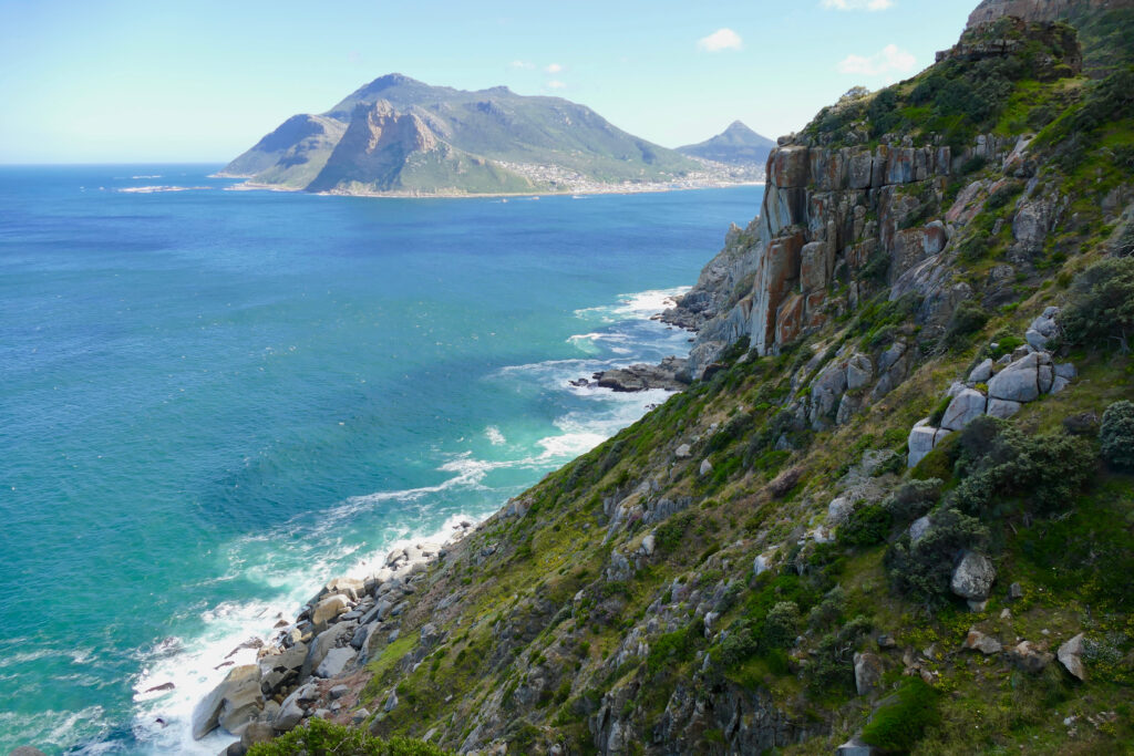 Vibrant coastal wallpaper with rugged rocks lush greenery turquoise sea and distant mountains