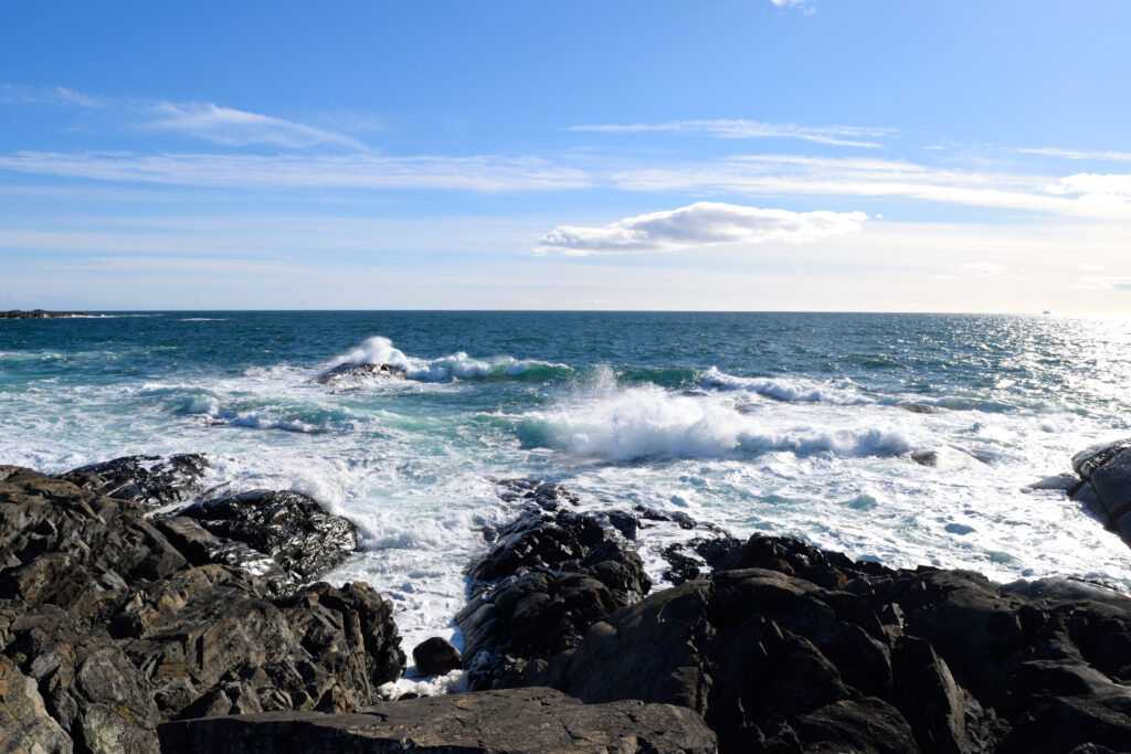 Coastal wallpaper with rugged rocks and crashing sea waves under clear blue sky background