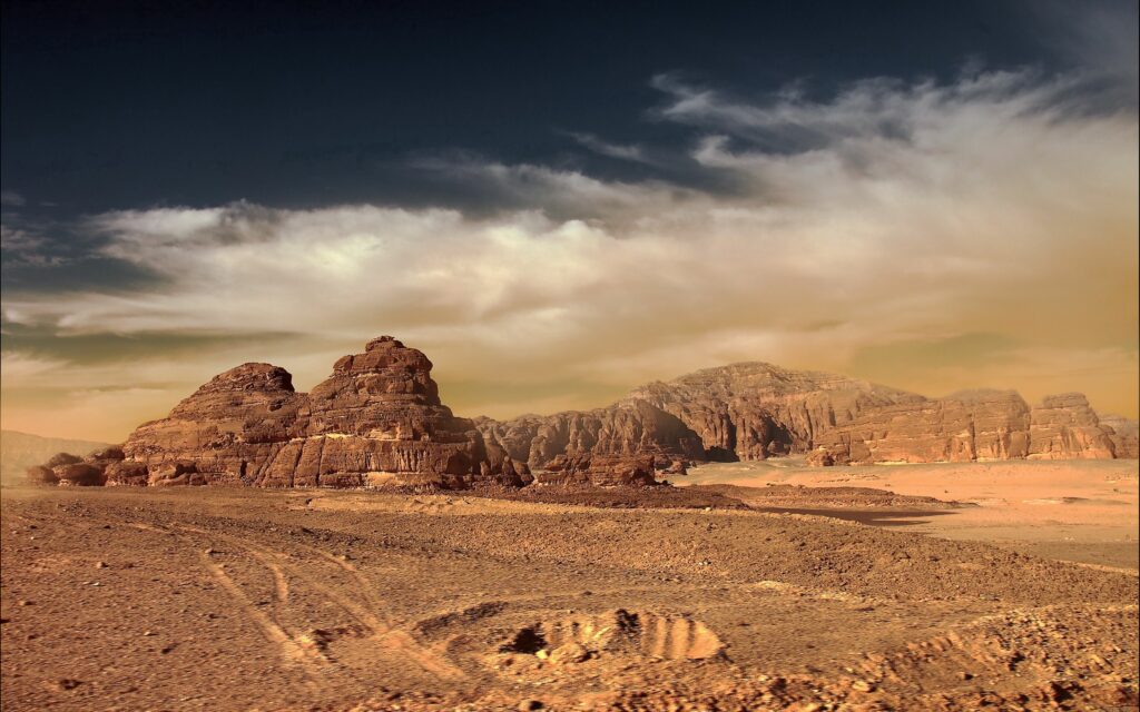 Desert landscape wallpaper with rugged sandstone mountains golden sand and dramatic cloudy sky