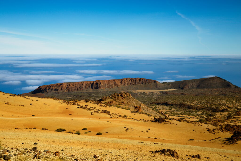 Desert landscape with rugged stone formations and golden sandy terrain under blue sky wallpaper