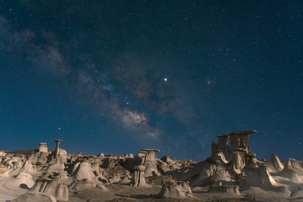 Starry night desert landscape with unique rock formations and Milky Way galaxy background wallpaper