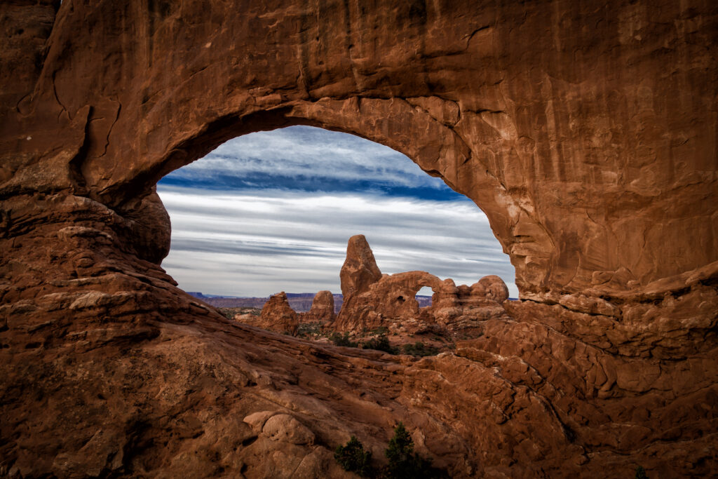 Massive natural stone arch in rugged red rock desert with layered formations and vivid sky Wallpaper